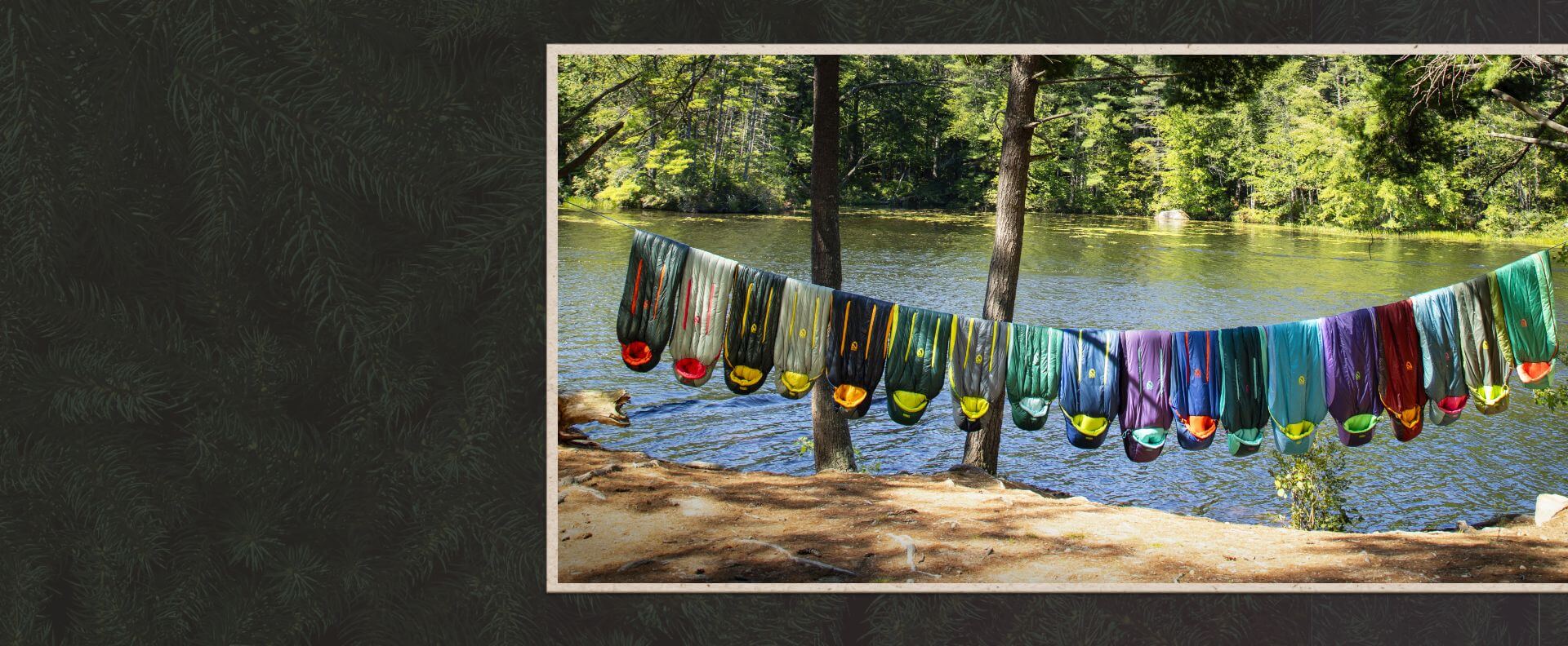 A group of sleeping bags hanging on a line near a body of water.